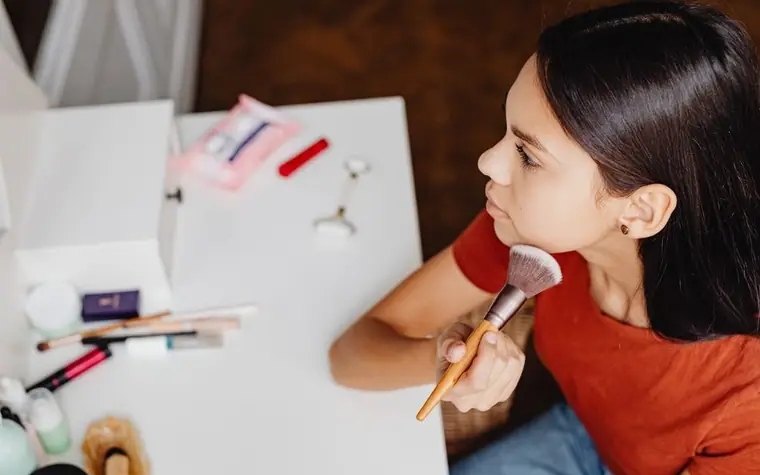 A woman applying face powder with a brush at a vanity mirror