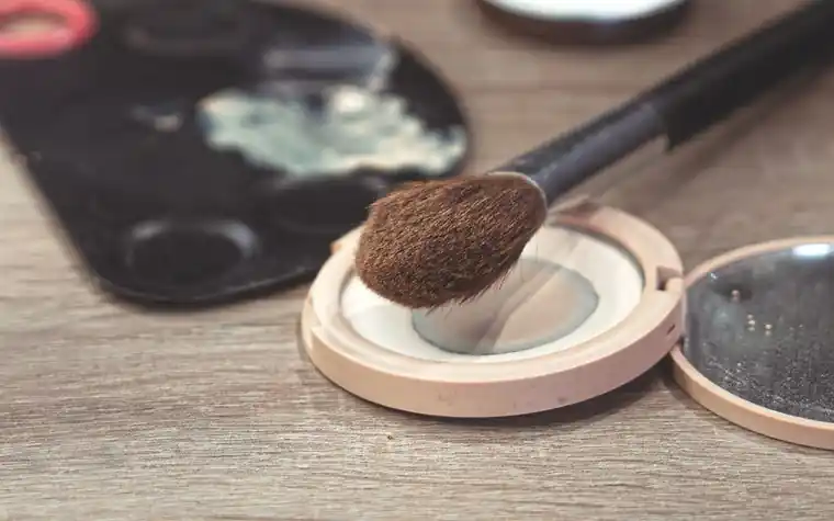 A makeup brush resting on an open pressed powder compact