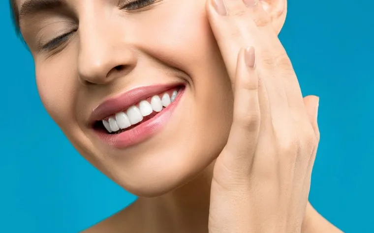 Close-up of a woman smiling with her eyes closed, touching her face