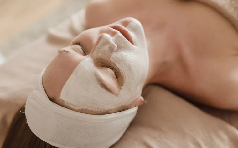 A woman with a clay face mask, relaxing during a skincare treatment