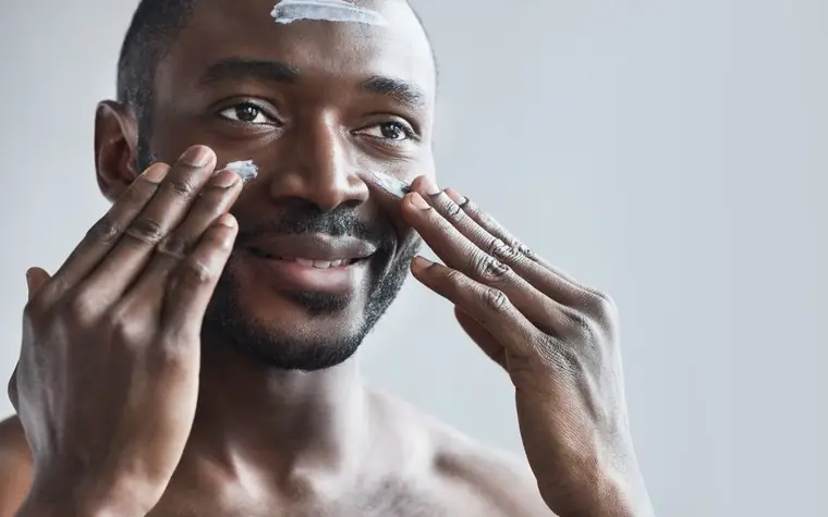 Man smiling while applying facial cream as part of a skincare routine