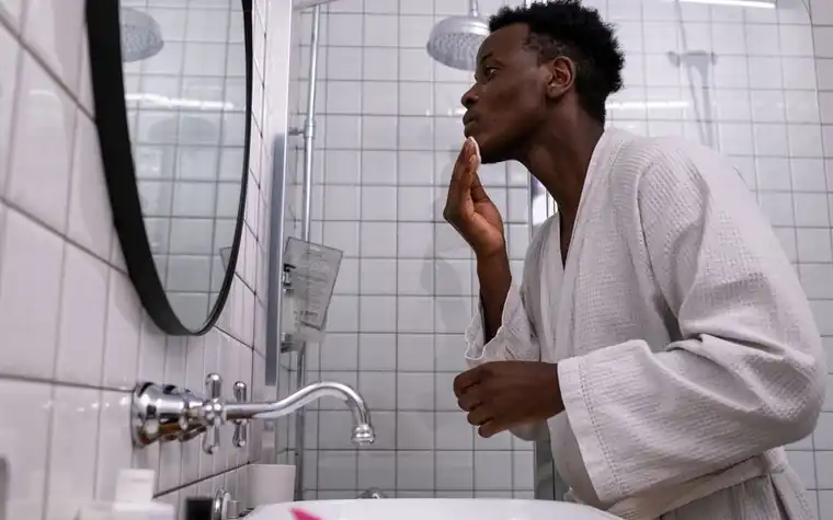 Man applying a skincare product to his face in a bathroom mirror
