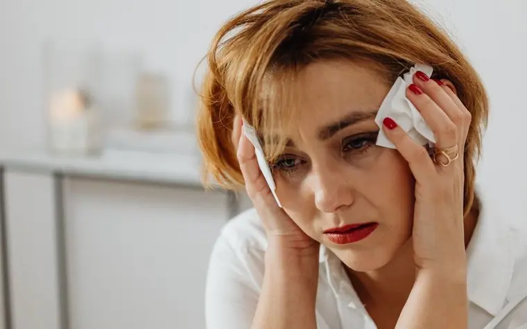 A woman pressing a tissue against her temple and cheek