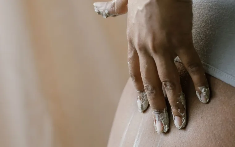A hand spreading pale cream across bare skin