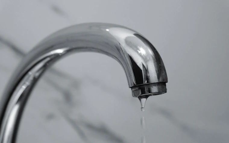 Chrome bathroom faucet with a thin stream of water against a marble wall