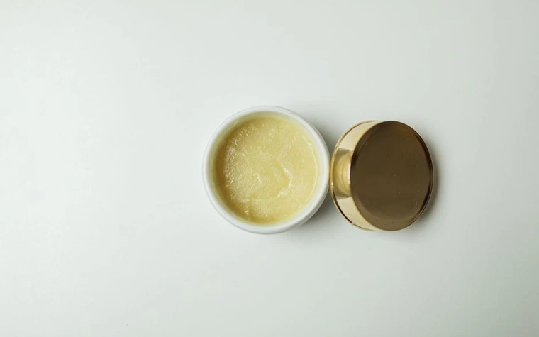 An open jar of white cream with a gold lid