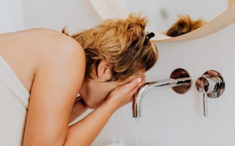 A woman washing her face with water at a bathroom basin