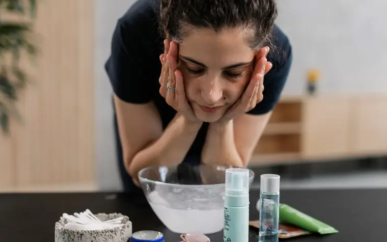 A woman cleansing her face beside an assortment of skincare products
