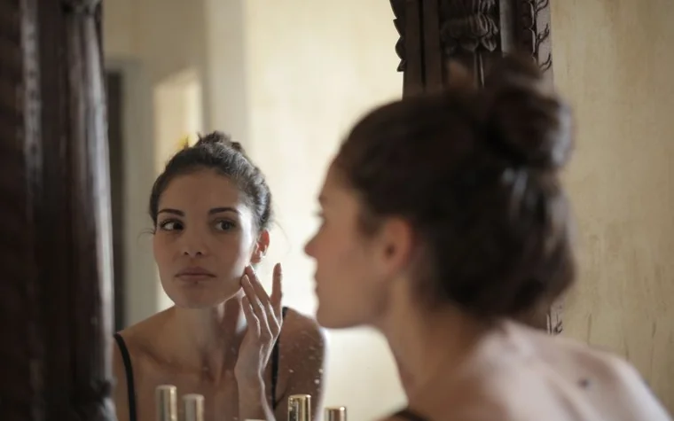 A woman examining her skin in a bathroom mirror