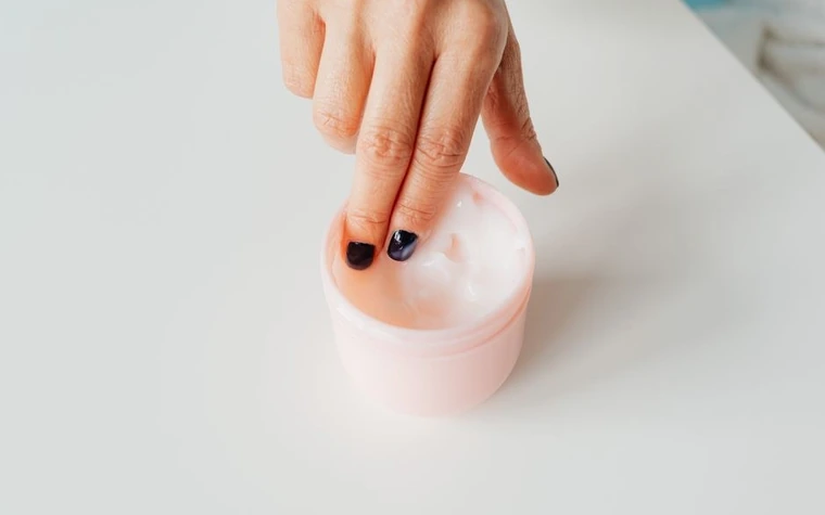A fingertip dipping into an open jar of white cream