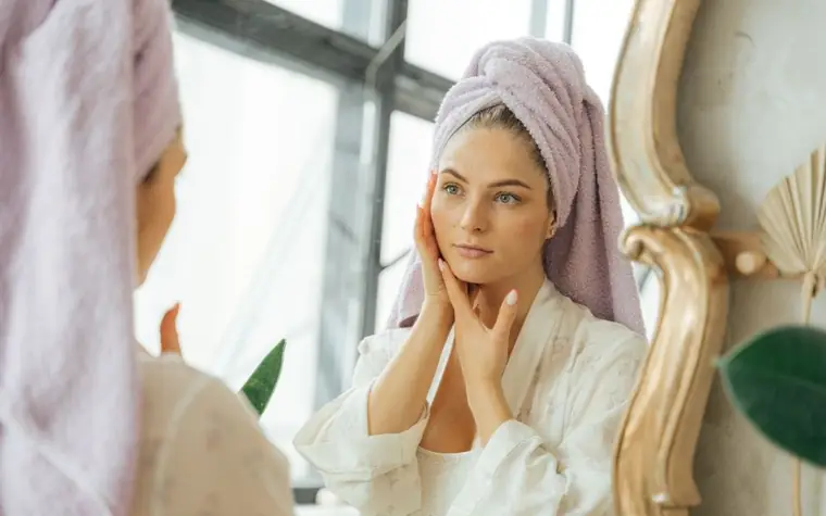 A woman with a hair towel touching her face near a window