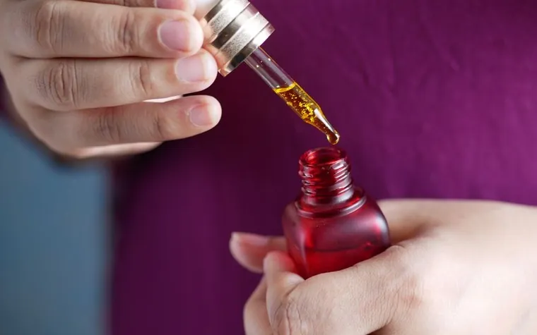 A hand holding a dropper above a serum bottle