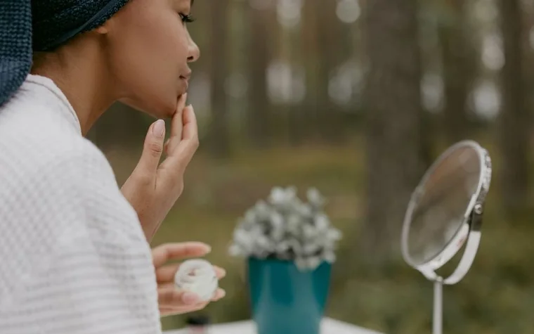 A woman touching her face while looking in a small mirror outdoors