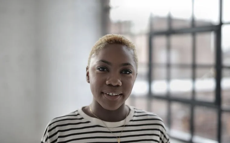 A smiling woman with clear skin standing by a window