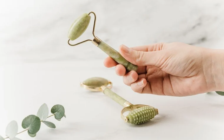 Hand holding a jade roller on marble with eucalyptus leaves