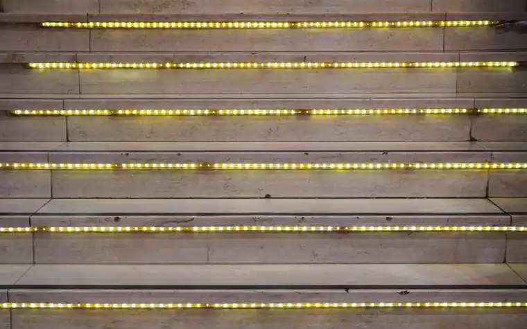 Rows of small amber LED lights running along stone stair edges in a dark space