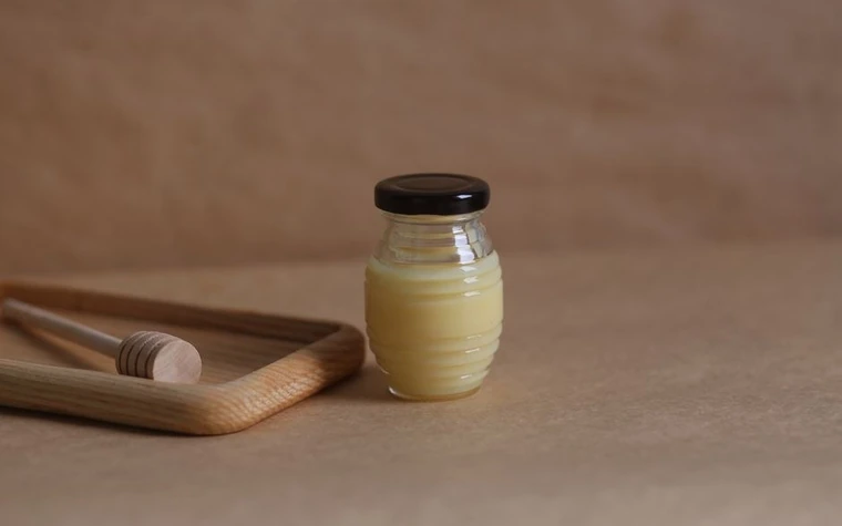 A small glass honey jar with a wooden lid on a wooden tray