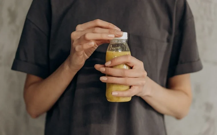 Close-up of a woman's hands opening a bottle of orange-colored beverage