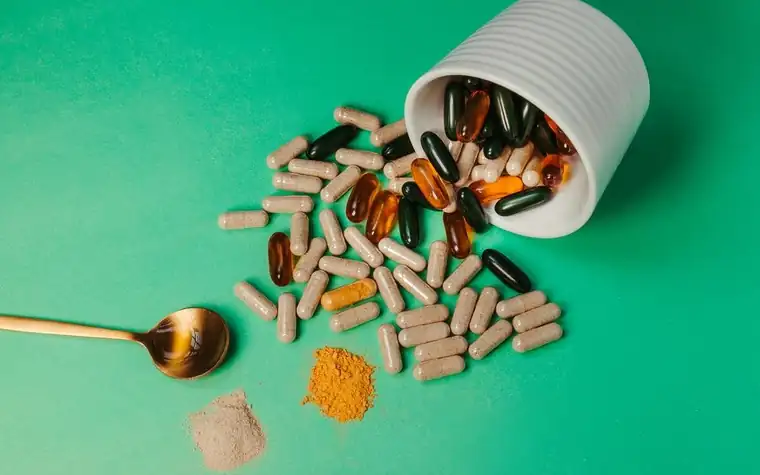 Capsules and powdered supplement spilling from a jar on a green background