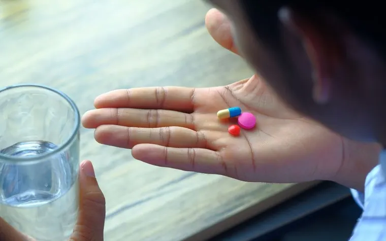 Hand holding colored supplement capsules next to a glass of water