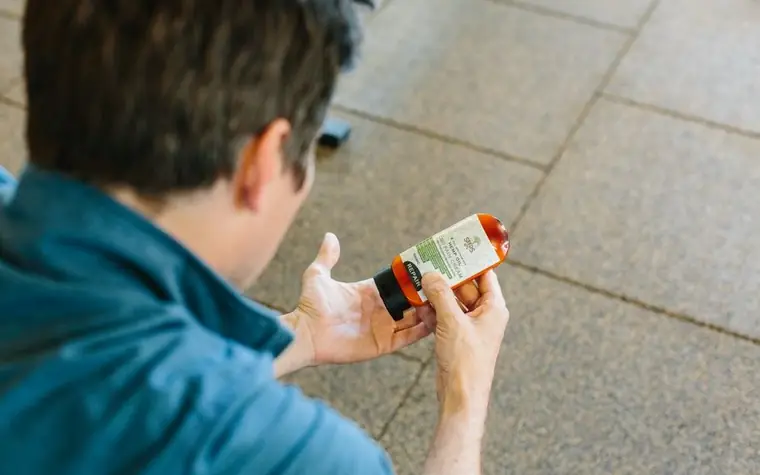 Man crouching outdoors reading the label on a small bottle held in his hand