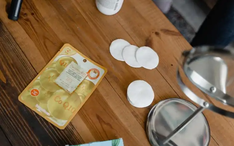 Cotton pads, a sheet mask and a hand mirror on a wooden table