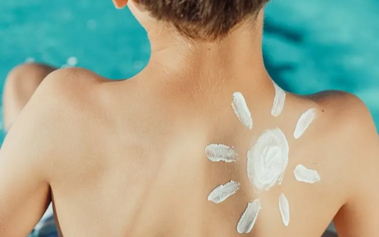 Child's bare back with a sun shape drawn in white sunscreen cream against a turquoise background