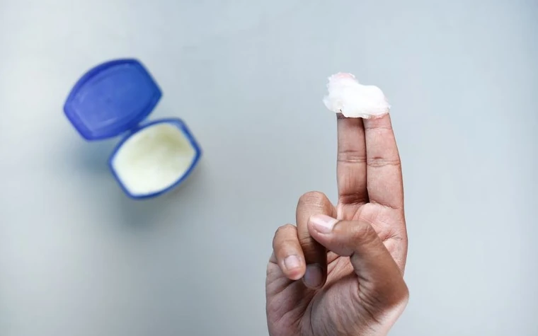 A fingertip holding a small amount of clear white ointment