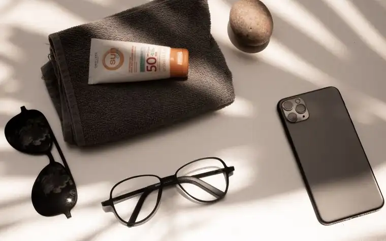 A flat lay of a sunscreen tube with sunglasses and a folded towel