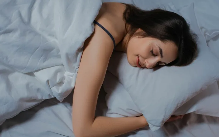 A woman sleeping peacefully in bed under white linens